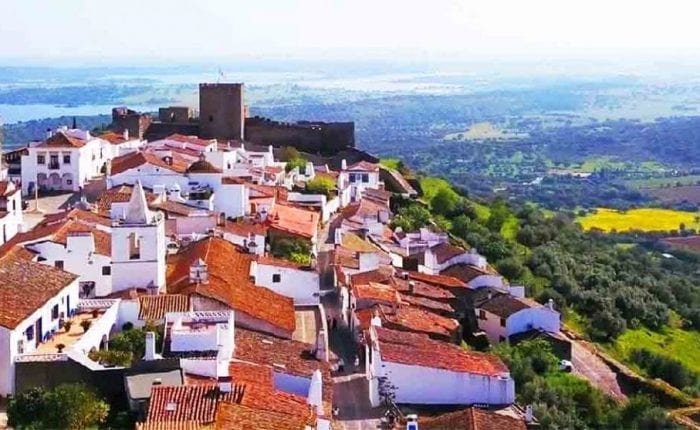 Aerial view of Monsaraz village in the Alentejo region of Portugal, with whitewashed houses, cobblestone streets, and Alqueva Lake in the background.