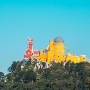 tunning view of Pena Palace in Sintra, Portugal, showcasing its vibrant red and yellow facade against the lush greenery of the Sintra Mountains. Explore this iconic landmark with Premiere Tours, offering personalized, private tours for an unforgettable experience.