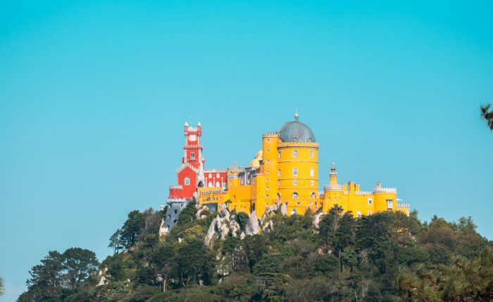 tunning view of Pena Palace in Sintra, Portugal, showcasing its vibrant red and yellow facade against the lush greenery of the Sintra Mountains. Explore this iconic landmark with Premiere Tours, offering personalized, private tours for an unforgettable experience.